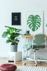 Stylish and modern scandinavian interior of office desk with mock up poster frames, a lot of plants , design office accessories and lamp. Cozy decor of freelancer room.