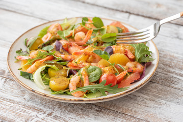 salad with shrimps and assorted salads (arugula, cherry tomatoes, chard, spinach) on white wooden background