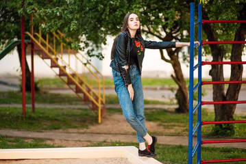 Portrait young punk rock fashion girl in black leather jacket with stiletto in a street warehouse urban environment, woman in jeans in the park