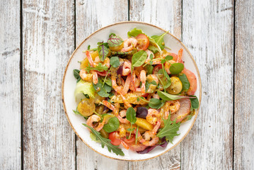 salad with shrimps and assorted salads (arugula, cherry tomatoes, chard, spinach) on white wooden background