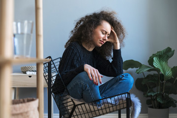Dark hair teenager with depression sitting alone on the armchair in gray room. Sadness, nostlagic,...