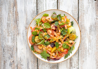 salad with shrimps and assorted salads (arugula, cherry tomatoes, chard, spinach) on white wooden background