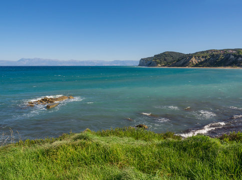 View on agios stefanos beach and bay with lush green grass and steep cliffs, north east coast of Corfu in Greece, summer day blue sky