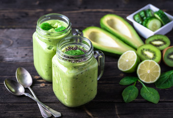 Green smoothie on dark background with avocado, spinach, lemon and kiwi on the right side.
