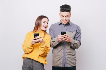 Young cheerful couple holding smartphones in their hands on white background. Girl looking in her...