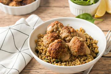 Spicy meatballs with spinach and bulgur in white bowl on wooden kitchen table.