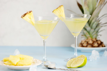 Two glasses with pineapple drink. Glasses are decorated with slices of pineapple and lime. In the background pineapple. Light background. Close-up. 
