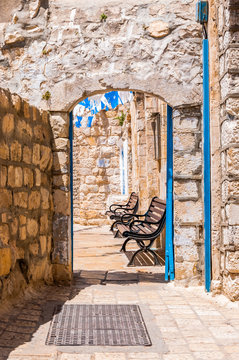Safed Old Town street, bystreet, alley, backstreet with benches, ancient stone walls, arcs and blue white decorations