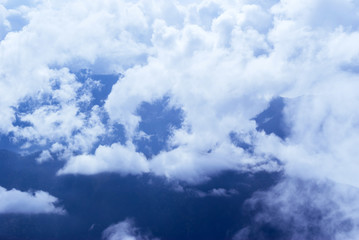view from above, from the peak or from an airplane, to a wooded mountain valley, partly hidden by cumulus clouds