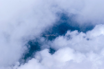 top view of white cumulus clouds; an settlement are visible in a small gap in the clouds