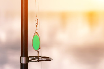 Fishing Reel And Green Spoon On A Background Of Water With Sunset Sunbeams closeup.