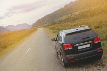 Plakat Black car SUV stands on the side of an asphalt road among the mountains. Travel by car through the mountain landscape. The rear of the vehicle with red lights in the foreground.