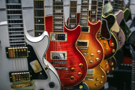 Picture of many electronic guitars hanging. They are different colors and shapes.