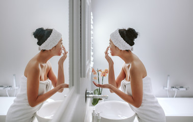 Woman in bathroom applying cosmetic on her face - obrazy, fototapety, plakaty