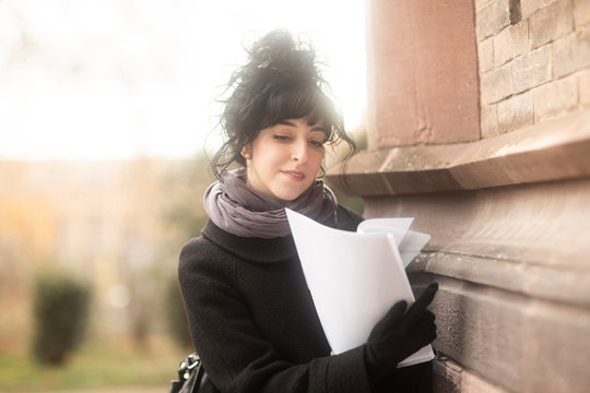 Woman standing by a wall looking at paperwork, Germany