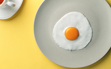 Simple breakfast on yellow background - Fried egg and cup of tea on yellow