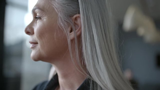 Close up of senior business woman standing in office and looking outside window. Mature business professional with grey hair looking away.