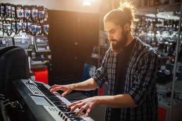Serious and concenrated young hipster sit and play on keyboard. He is alone in room. It is sunny inside.