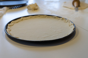 Preparation of a delicious pizza in a home kitchen. Laying and decorating pizza dough on the kitchen table.