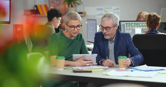 Two experienced designers discussing prototype brainstorming project in cozy office.