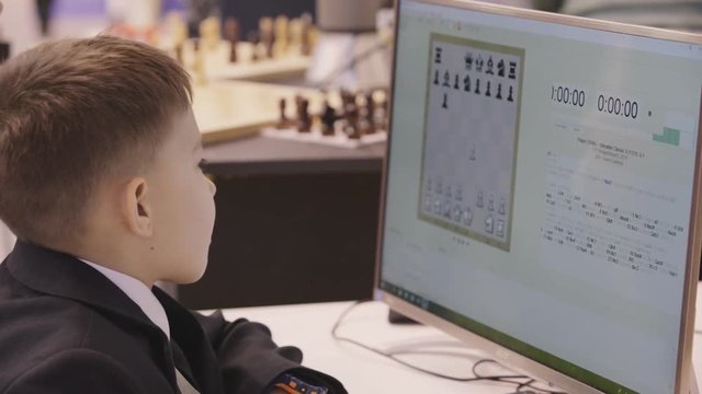 4k Russia, Moscow, November 28, 2018. Smart school boy playing chess with copmputer, chess robot. Child genius concept.