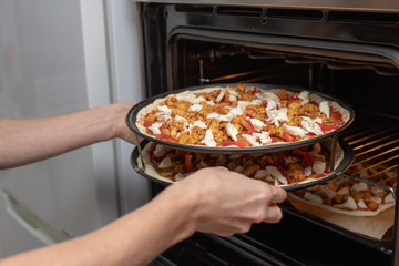 Preparation of a delicious pizza in a home kitchen. Laying and decorating pizza dough on the kitchen table.