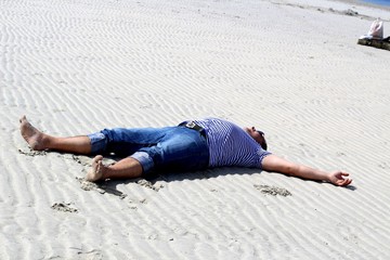 The man in clothes lies on white sand on the beach