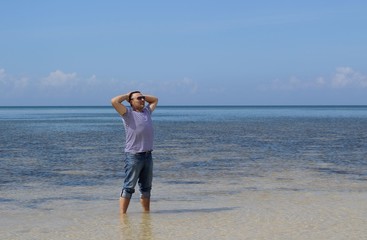 A man stands in the sea in the Philippines and with his hands behind his head looking thoughtfully into the distance