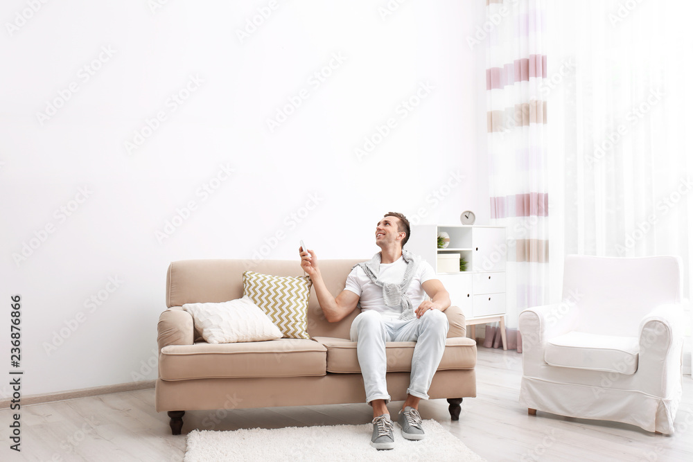 Canvas Prints happy young man operating air conditioner with remote control at home