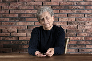Poor elderly woman counting coins at table