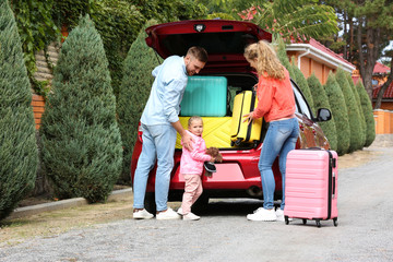 Young family loading suitcases in car trunk outdoors © New Africa