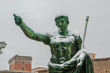 Frozen roman emperor. Caesar Augustus bronze statue along Imperial Forum covered by snow, a very...