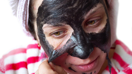 Young woman. Black cosmetic mask on the face. White background. Close-up portrait. A towel on your head. Wearing a housecoat. Design element.