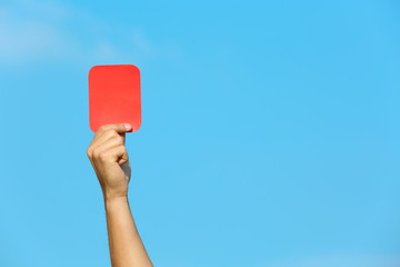Football referee showing red card against blue sky, closeup with space for text