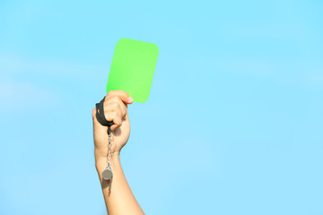 Football referee showing green card against blue sky, closeup with space for text