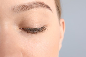 Young woman with beautiful natural eyelashes on gray background, closeup