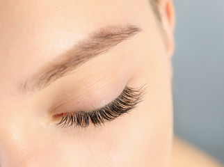 Young woman with beautiful long eyelashes on gray background, closeup. Extension procedure
