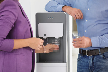 Employees taking glasses of water from cooler in office, closeup