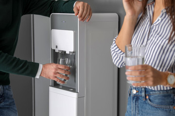 Young man taking glass of water from cooler in office, closeup