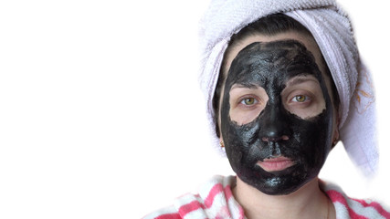 Young woman. Black cosmetic mask on the face. White background. Close-up portrait. A towel on your head. Wearing a housecoat. Design element.
