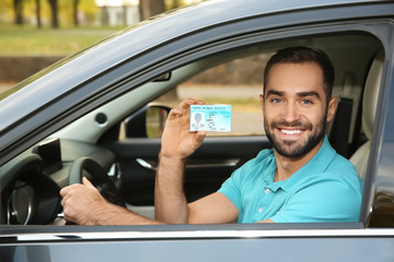 Young man holding driving license in car