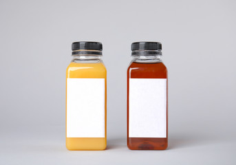 Tasty drinks in bottles with blank labels on color background. Mock up for design