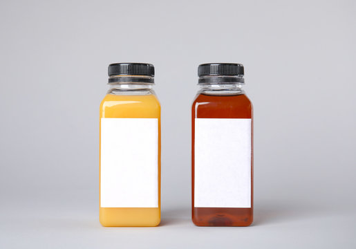 Tasty drinks in bottles with blank labels on color background. Mock up for design