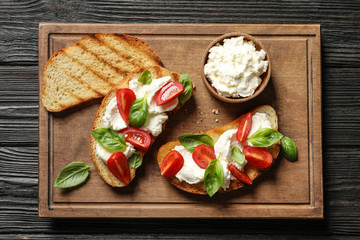 Toasted bread with tasty cream cheese and tomatoes on wooden table, flat lay