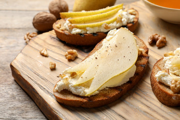 Toasted bread with tasty cream cheese and pear on wooden board