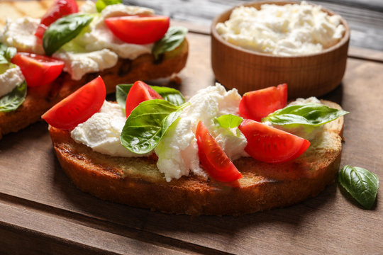 Toasted bread with tasty cream cheese and tomatoes on wooden board