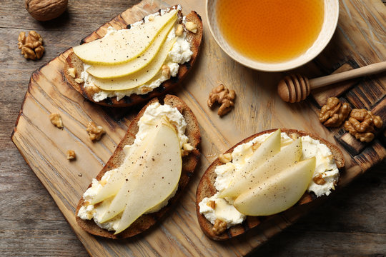 Toasted bread with tasty cream cheese and pear on wooden table, flat lay