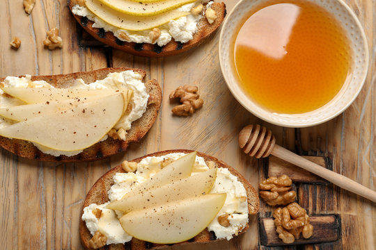 Toasted bread with tasty cream cheese and pear on wooden table, flat lay