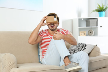 Young man using cardboard virtual reality headset at home