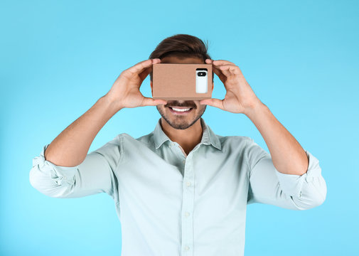 Young man using cardboard virtual reality headset on color background